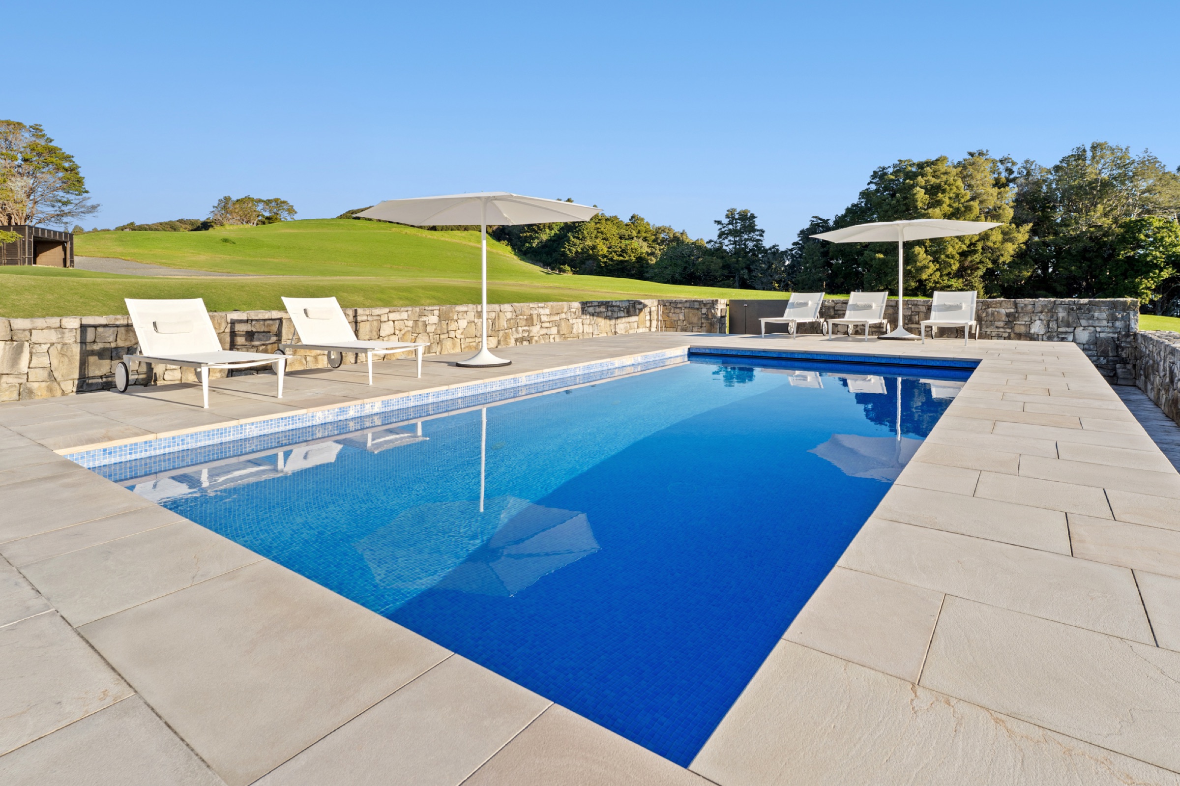 The pool at Bluestone Encampment: blue mosaic tiles, stone walls, white loungers and umbrellas, and the lawn rising to the bush behind.