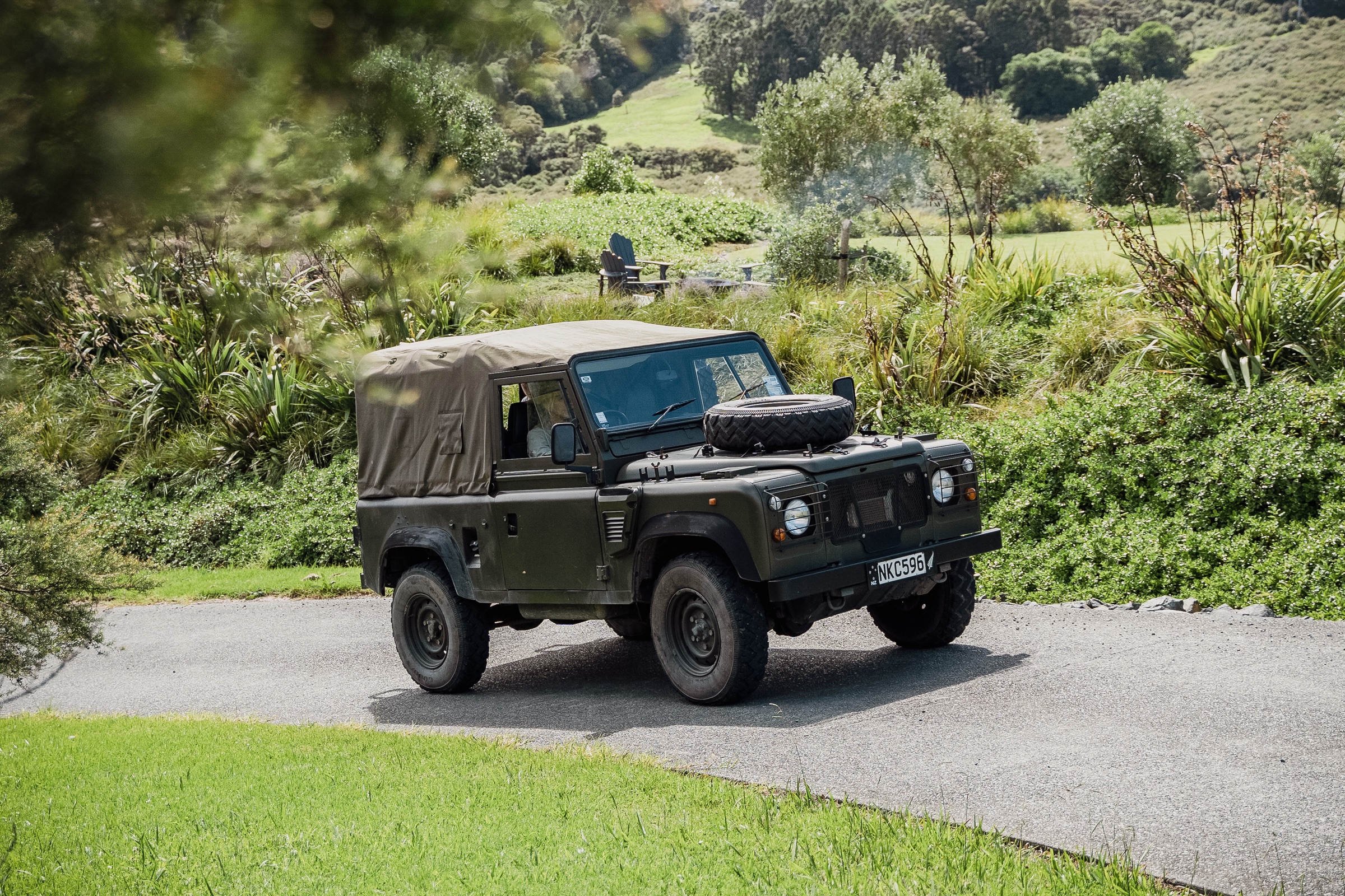 The estate's canvas-topped Land Rover Defender on the drive at Bluestone Estate, flax and native bush behind, the firepit and Adirondack chairs on the rise beyond.