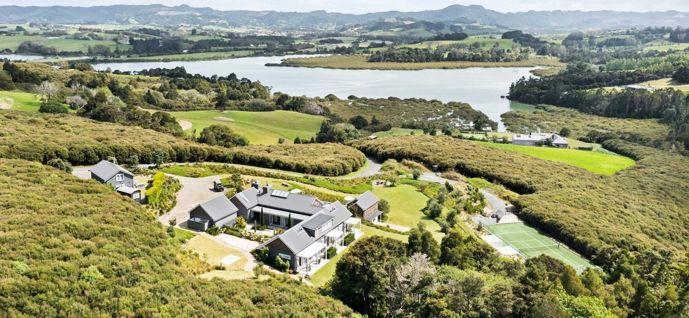 Bluestone Main Estate from the air: the Main House, pool, and tennis court above the Matakana estuary on the Tāwharanui Peninsula.