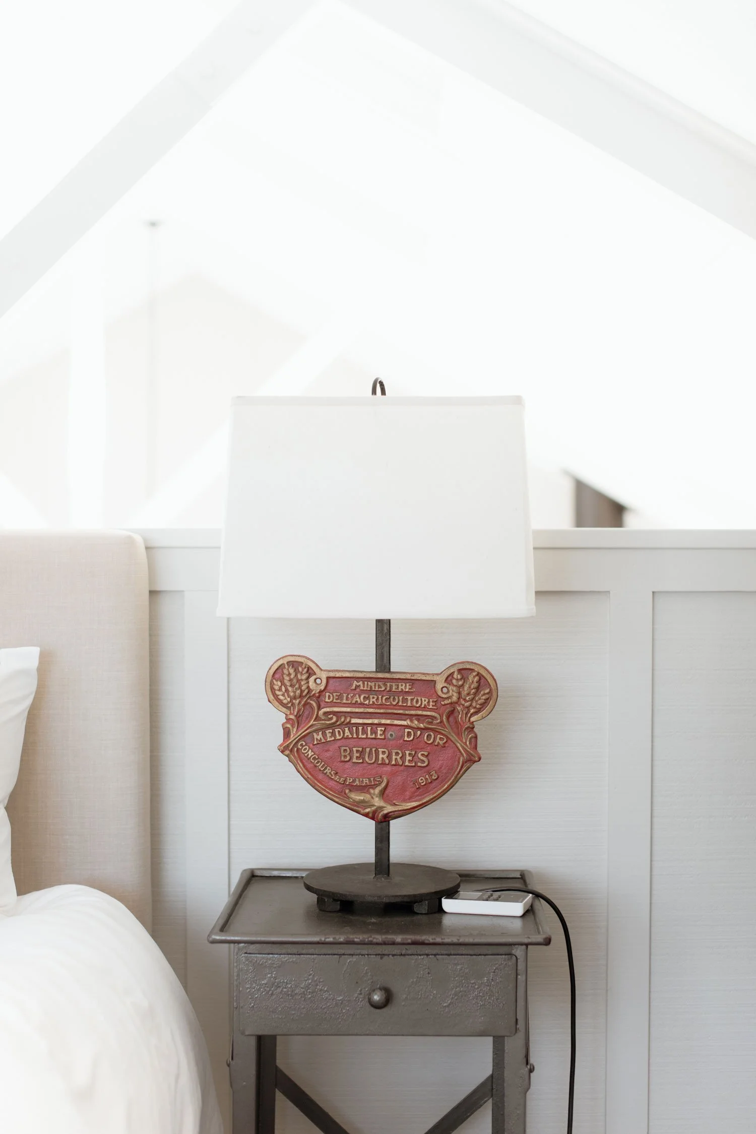The loft bedroom in the Boat House at Bluestone Estate: bedside table and lamp under the white timber ceiling.