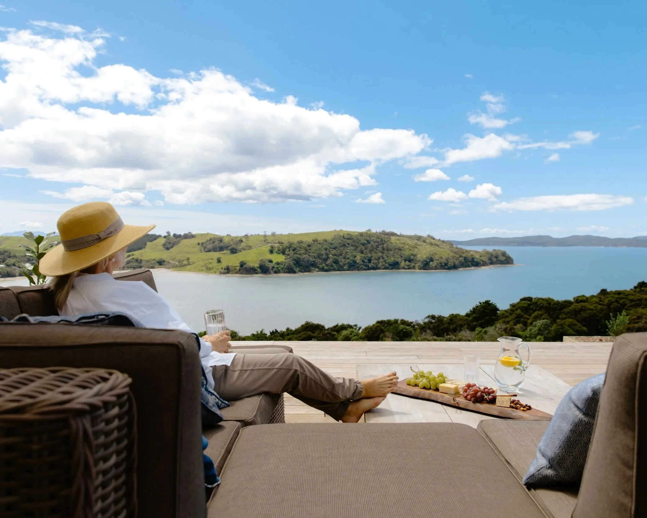 A guest in a straw hat on the Farmhouse deck at Bluestone Ridge, with a grazing platter and the Gulf view.