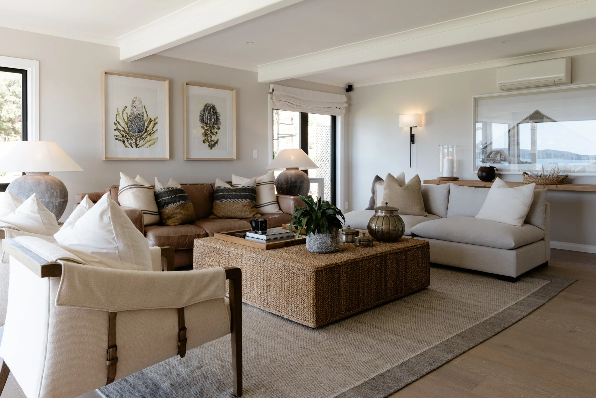The Farmhouse living room at Bluestone Ridge: tan leather sofa, linen armchairs, and botanical prints.