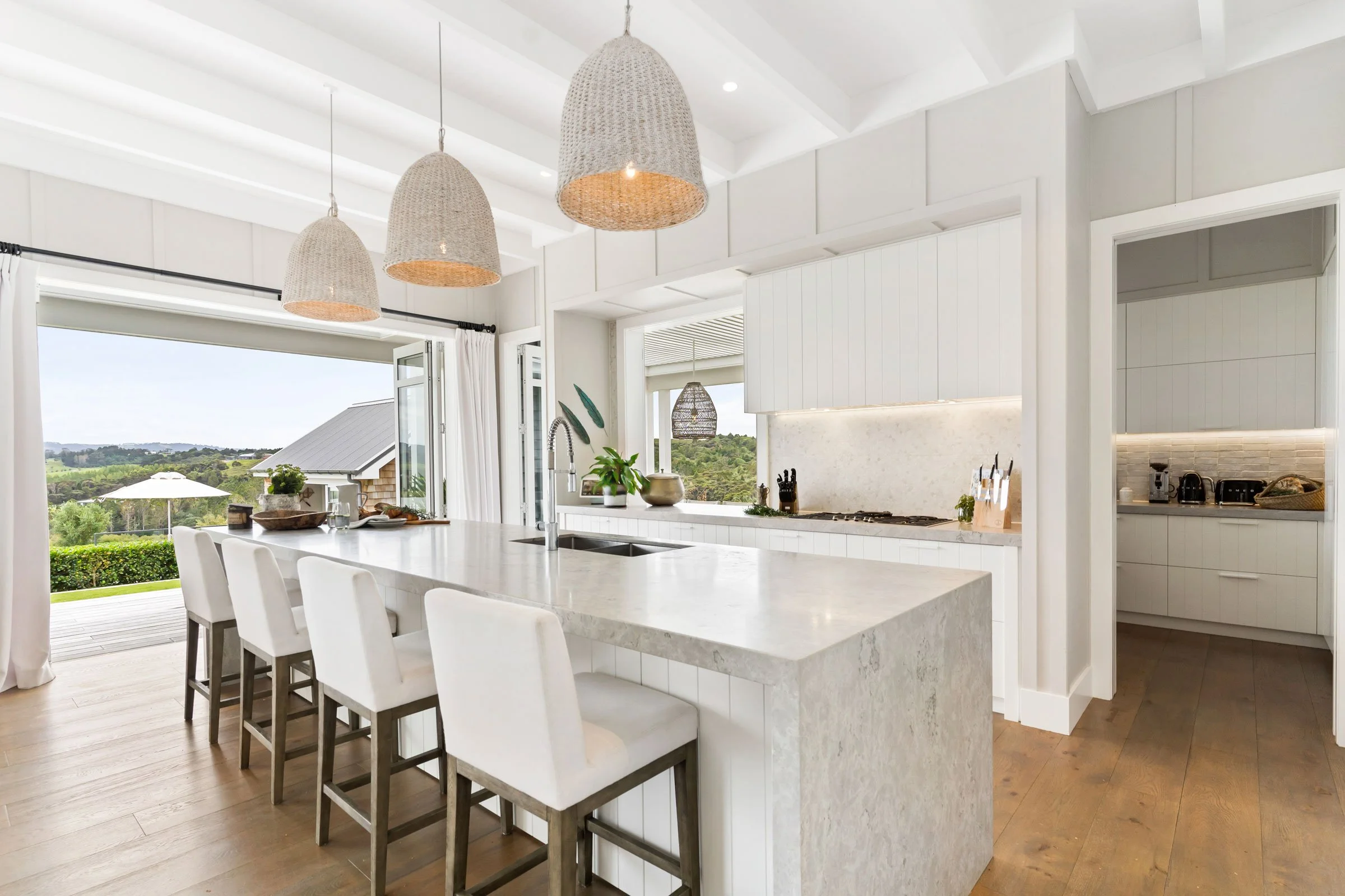 The Main House kitchen at Bluestone Estate: marble island, rattan pendants, and doors open to the pool.