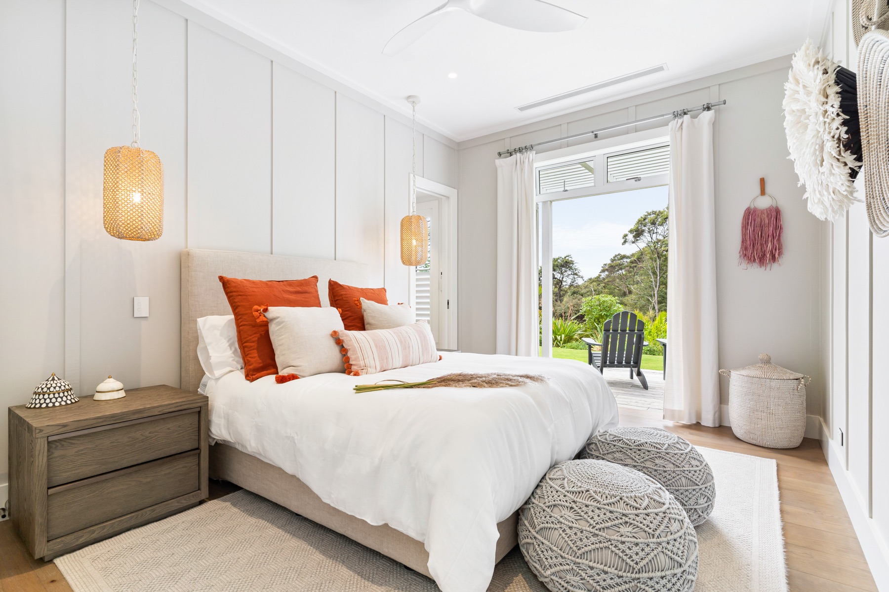 The Terracotta Bedroom at the Main House, Bluestone Estate: a queen bed with terracotta and blush cushions, rattan pendants, crochet poufs at its foot, and French doors open to the lawn and an Adirondack chair.