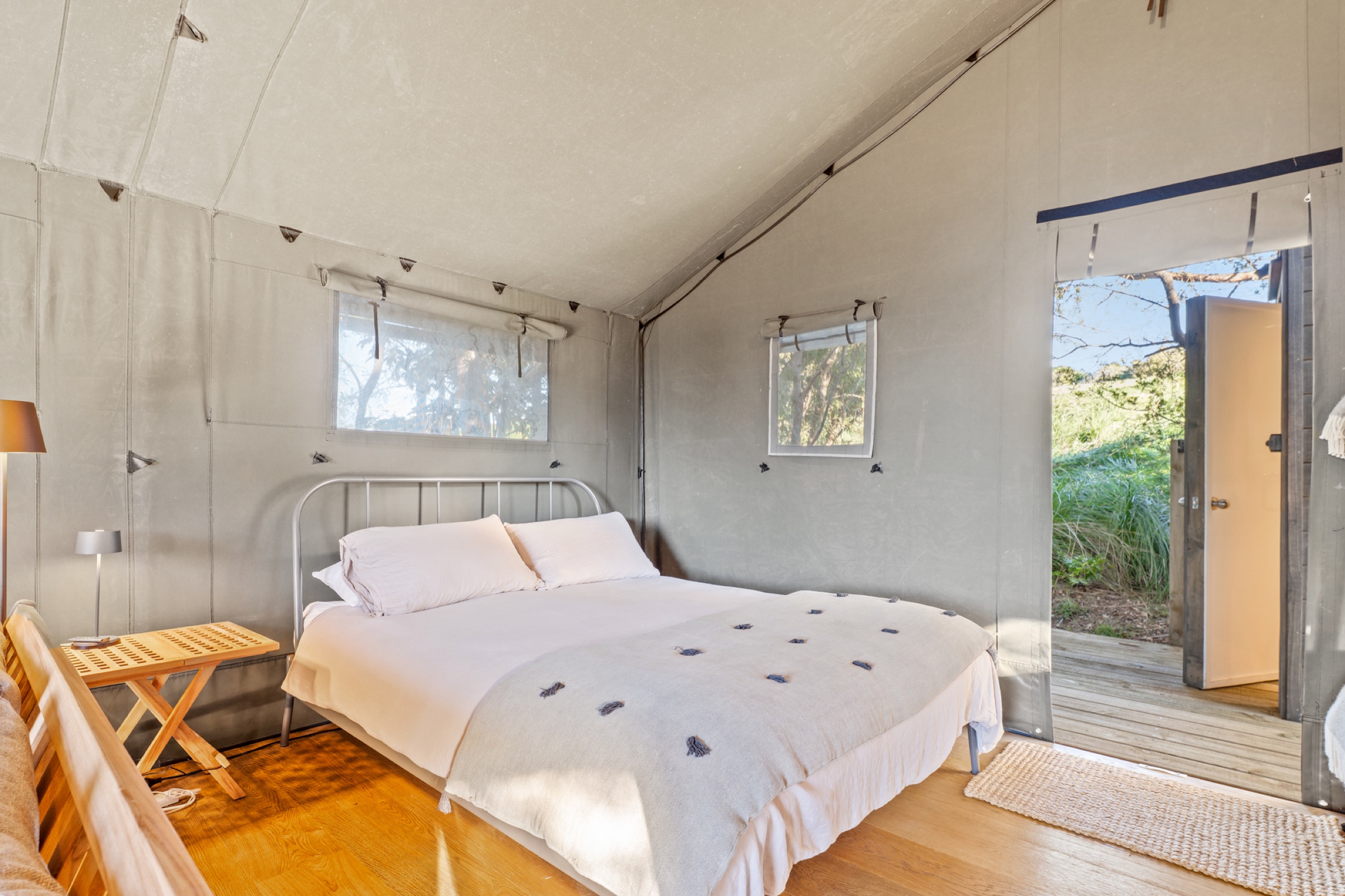 Inside Safari Tent 1 at Bluestone Encampment: the queen bed with white linen under the canvas, a timber floor, and the door open to the bush.