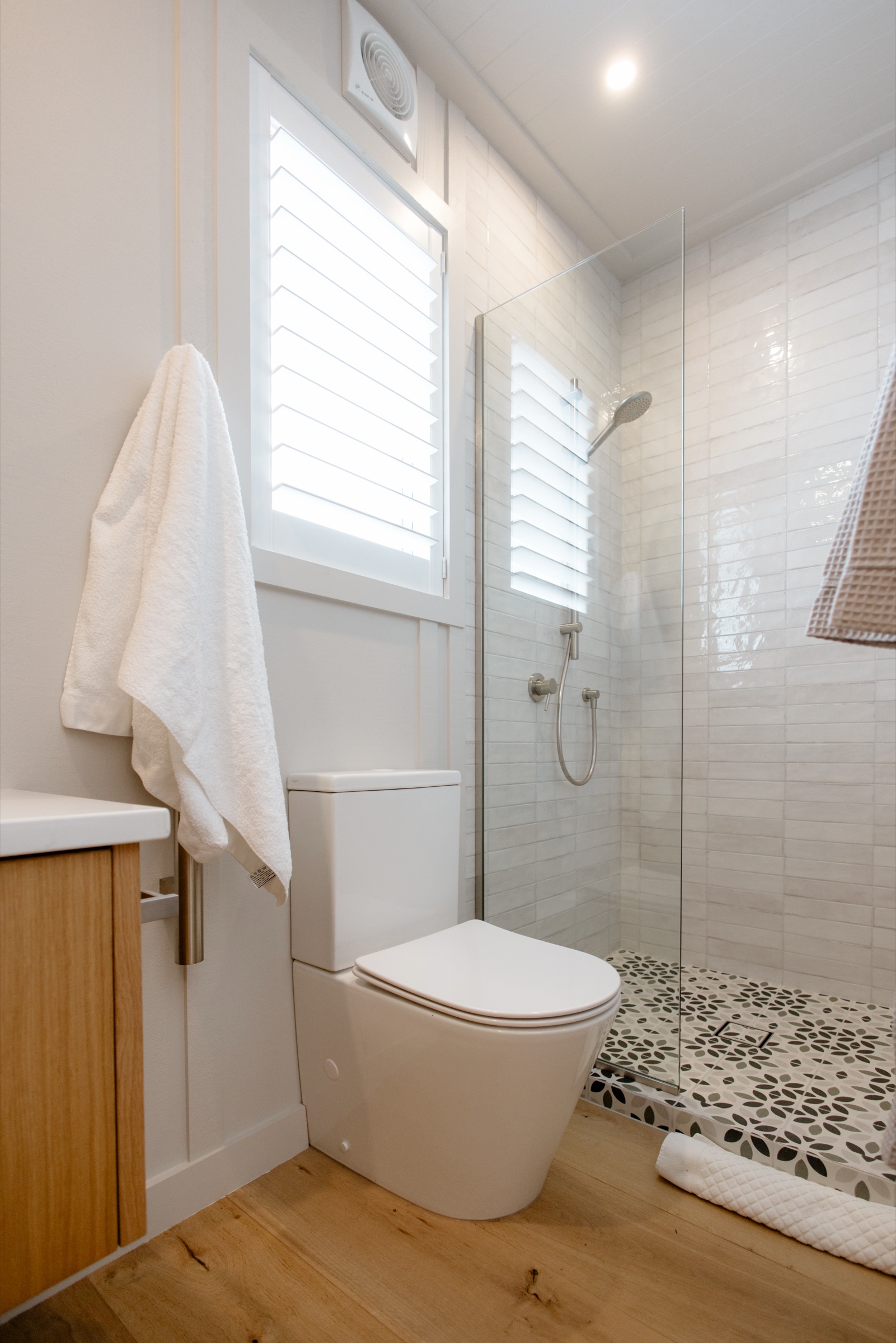 The Studio bathroom at Bluestone Estate: a glass-screened shower with white subway tiles and a patterned tiled floor, shutters at the window, and an oak vanity.