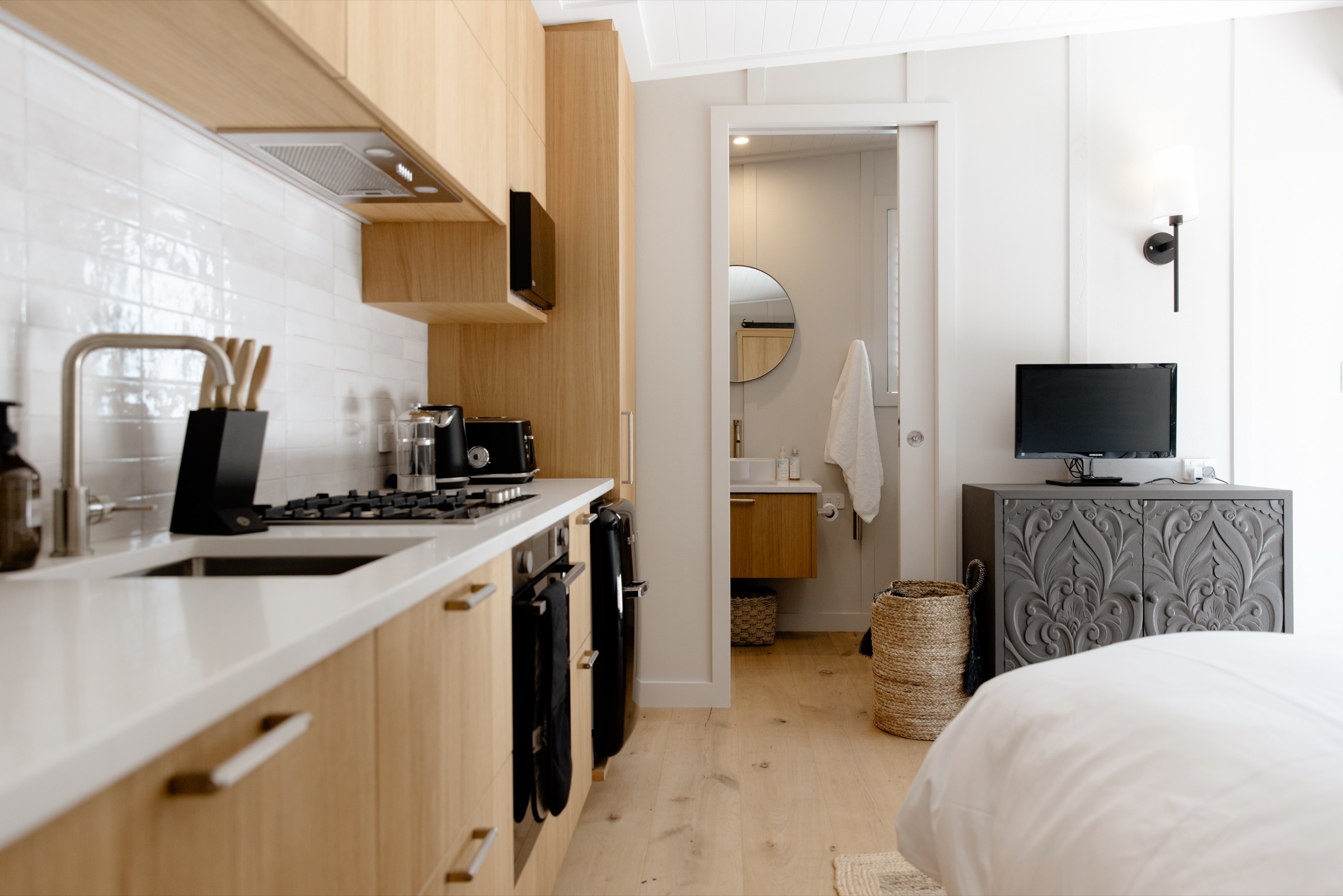Inside the Studio at Bluestone Estate: the oak kitchen with gas hob and oven, the bed with white linen, and the bathroom through the sliding door.