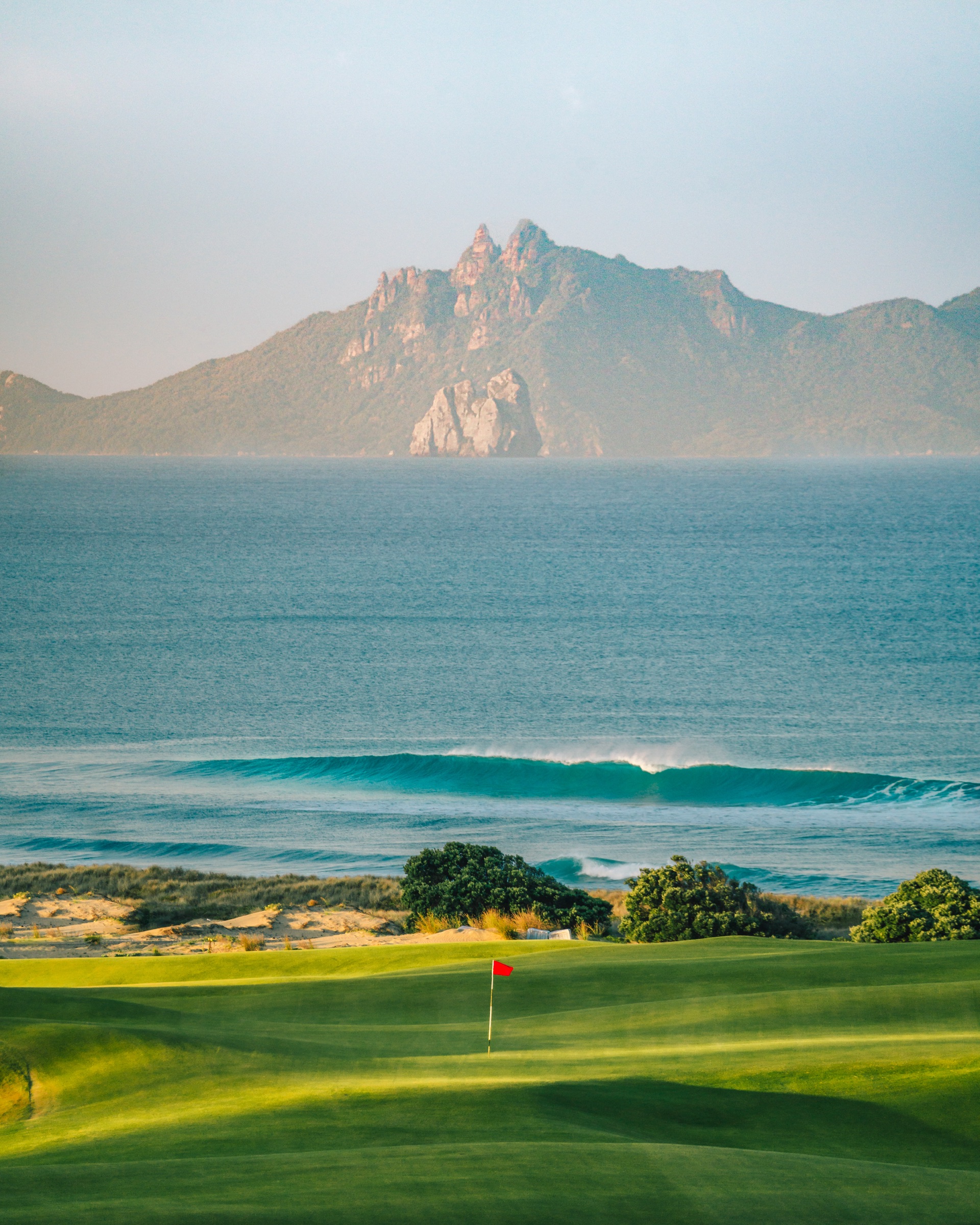 A green on the North Course at Te Arai Links, forty minutes from Bluestone Estate, with a wave breaking on the beach behind it and the Hen and Chicken Islands across the water.
