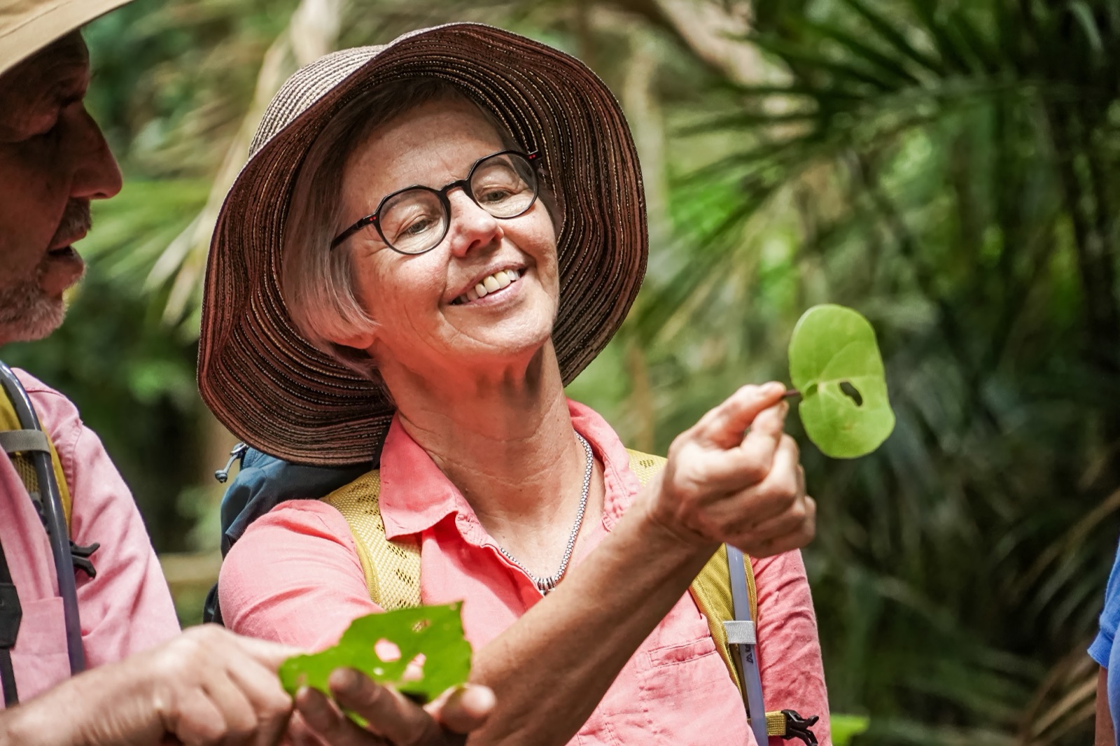 A guest in a wide-brimmed hat smiles as she holds up a heart-shaped kawakawa leaf on a Terra and Tide bush walk.