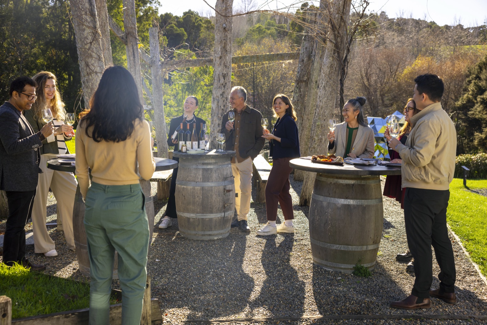 Guests standing at wine barrels under the trees for a Terra and Tide wine tasting at Brick Bay.